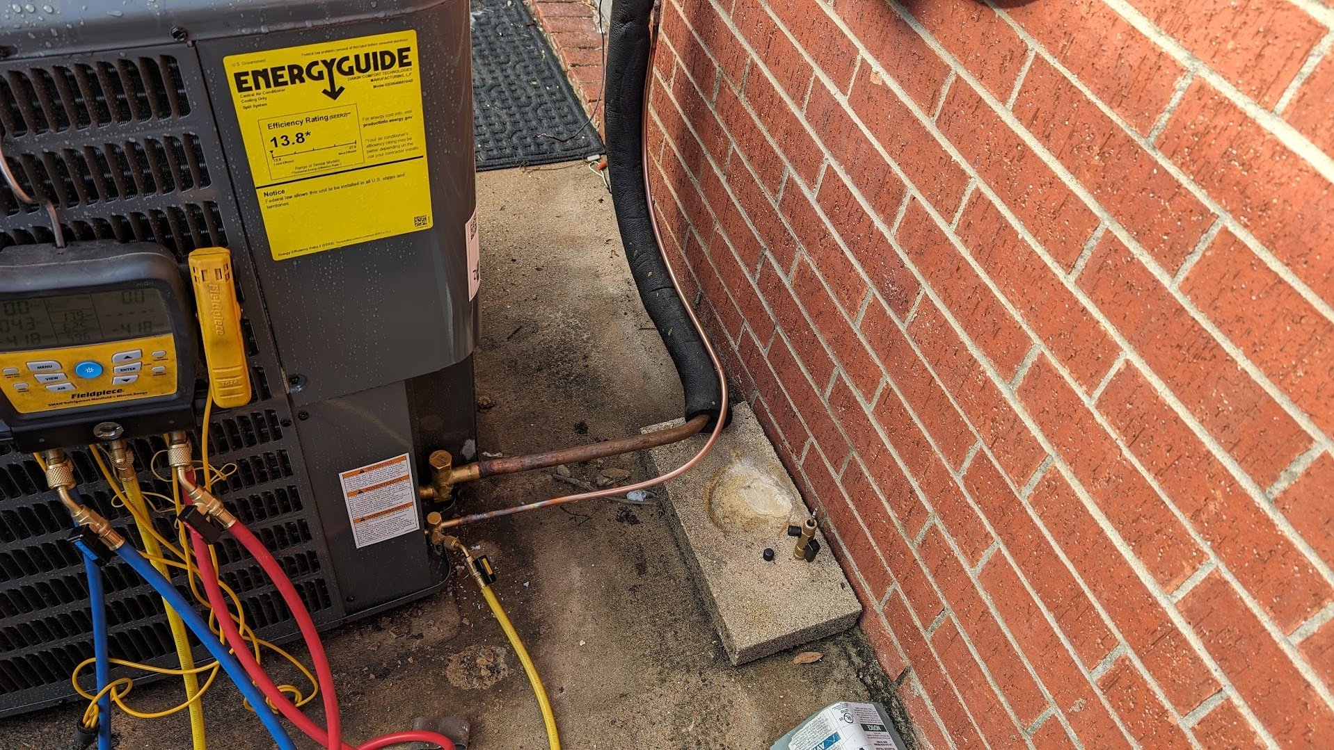 Outdoor AC unit with service gauges connected and copper refrigerant lines running to its valves